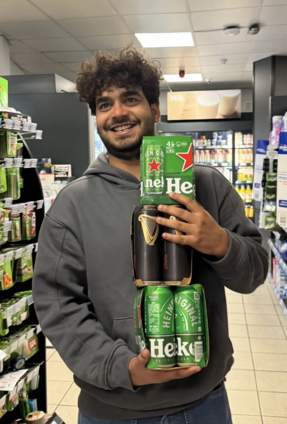Prateek smiling while holding several packs of beer in a shop