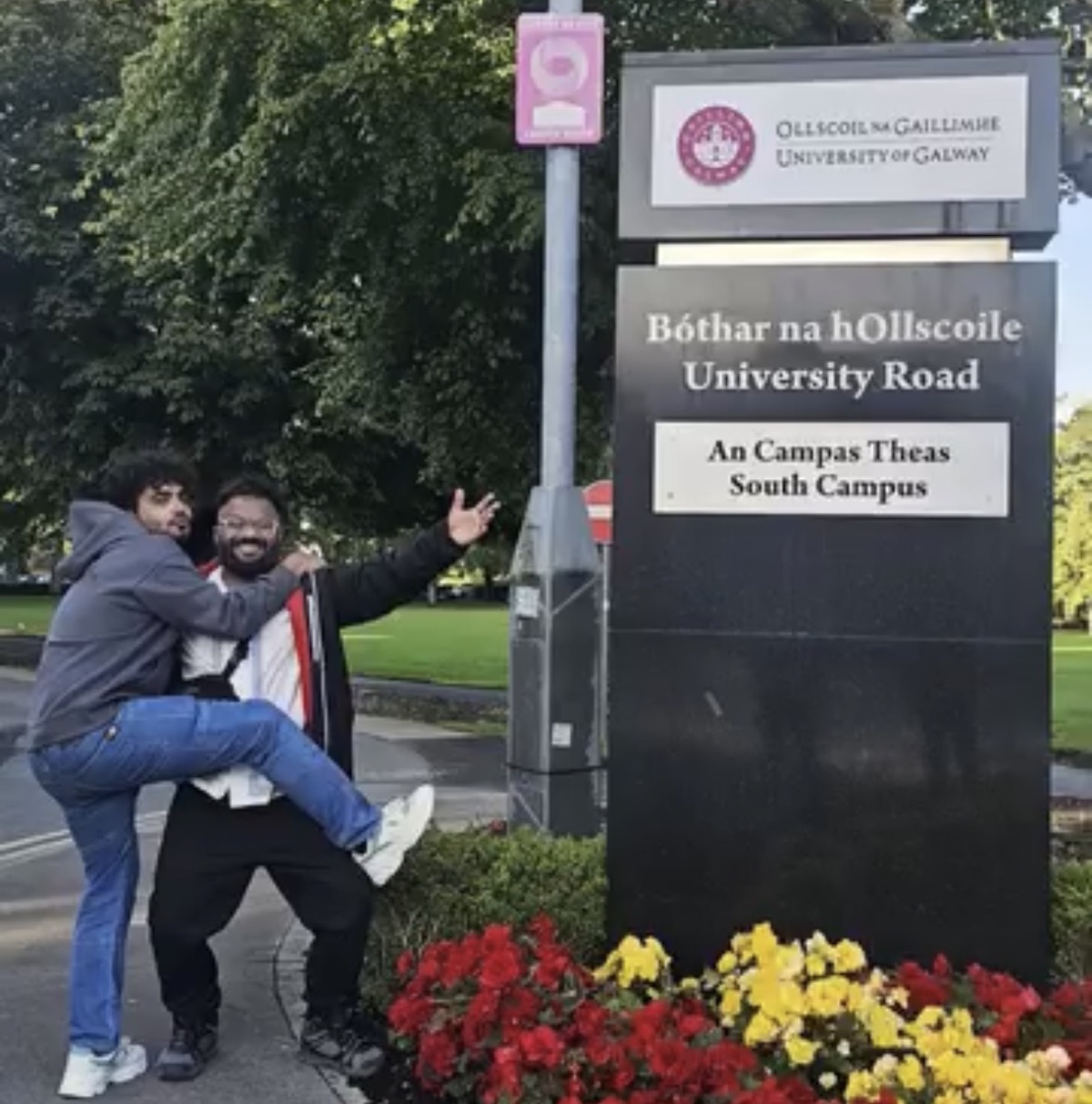 Two friends posing beside the University of Galway sign on University Road