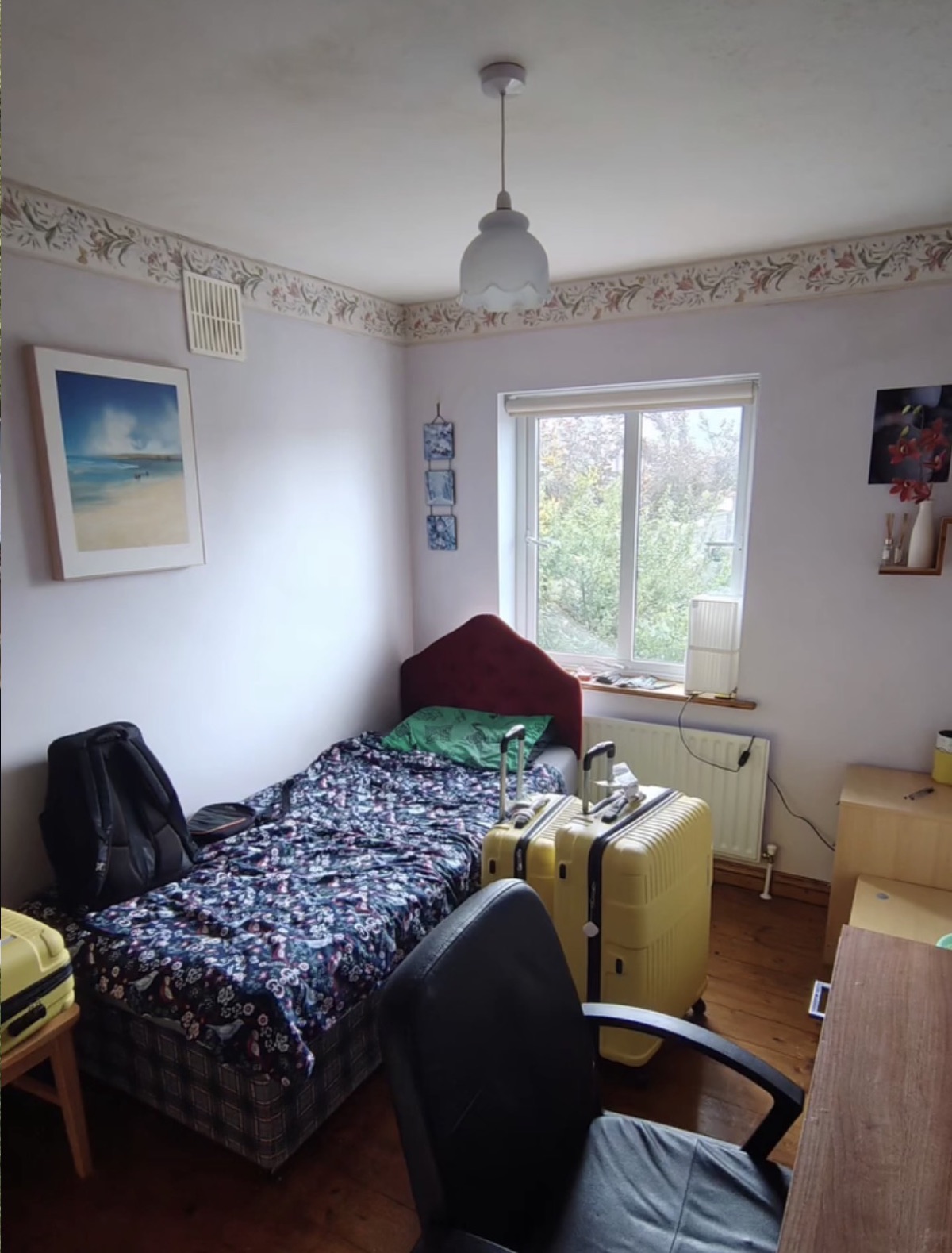A small bedroom with two suitcases, a single bed and a desk